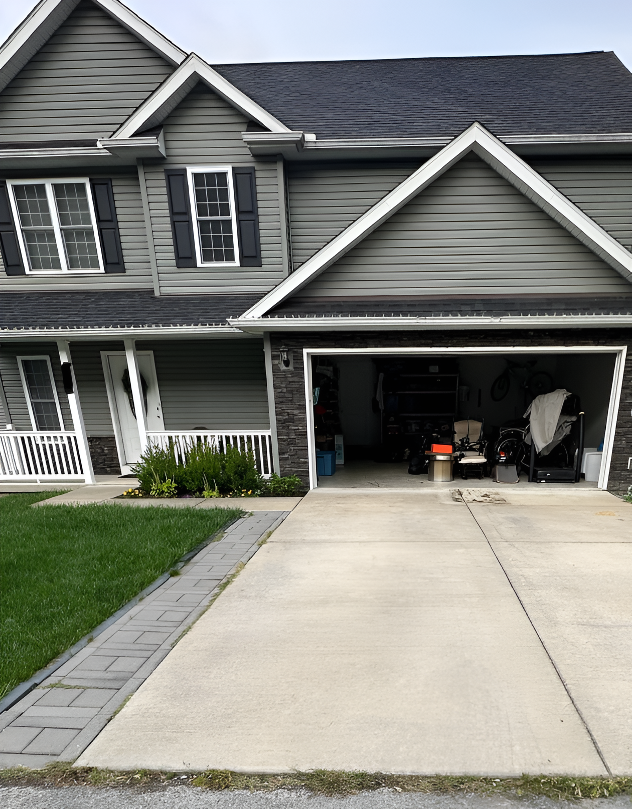 Suburban house with gray siding, front porch, and open garage beside a concrete driveway