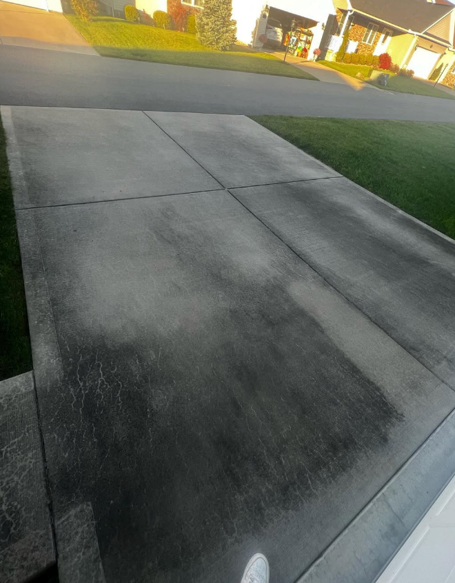Concrete driveway and sidewalk at dusk beside a grassy lawn and houses.