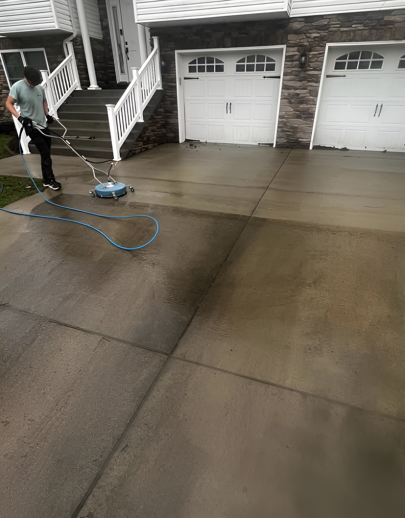 Person power-washing a concrete driveway outside white garage doors.