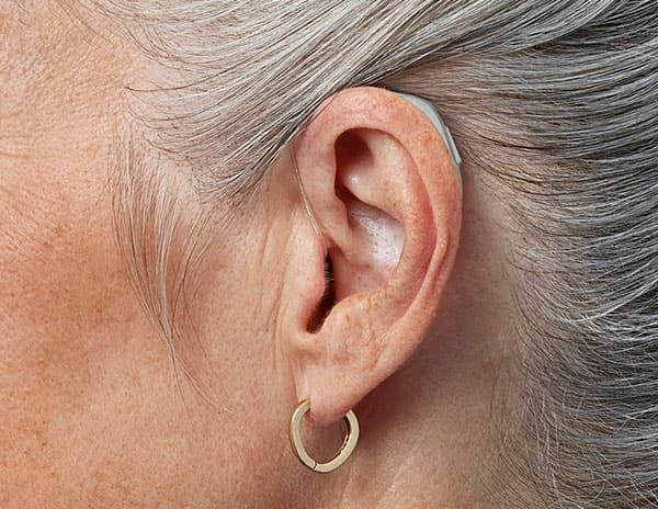 Una persona tiene in mano una custodia aperta contenente un apparecchio acustico retroauricolare beige.