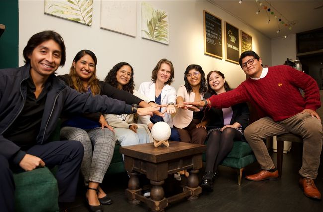 Un grupo de personas están sentadas alrededor de una mesa tomadas de la mano.