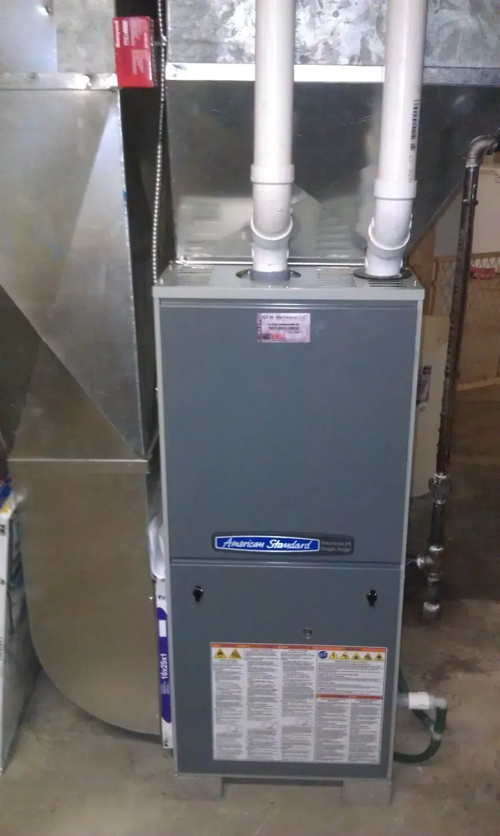 A furnace is sitting in a basement next to a duct.