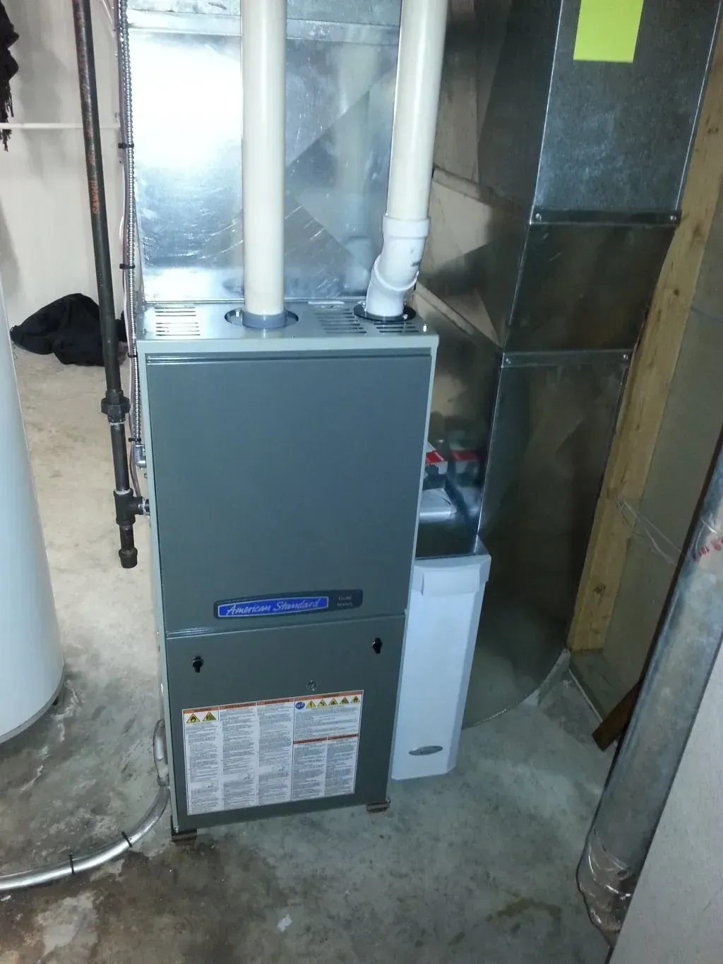 A furnace is sitting in a basement next to a water heater.