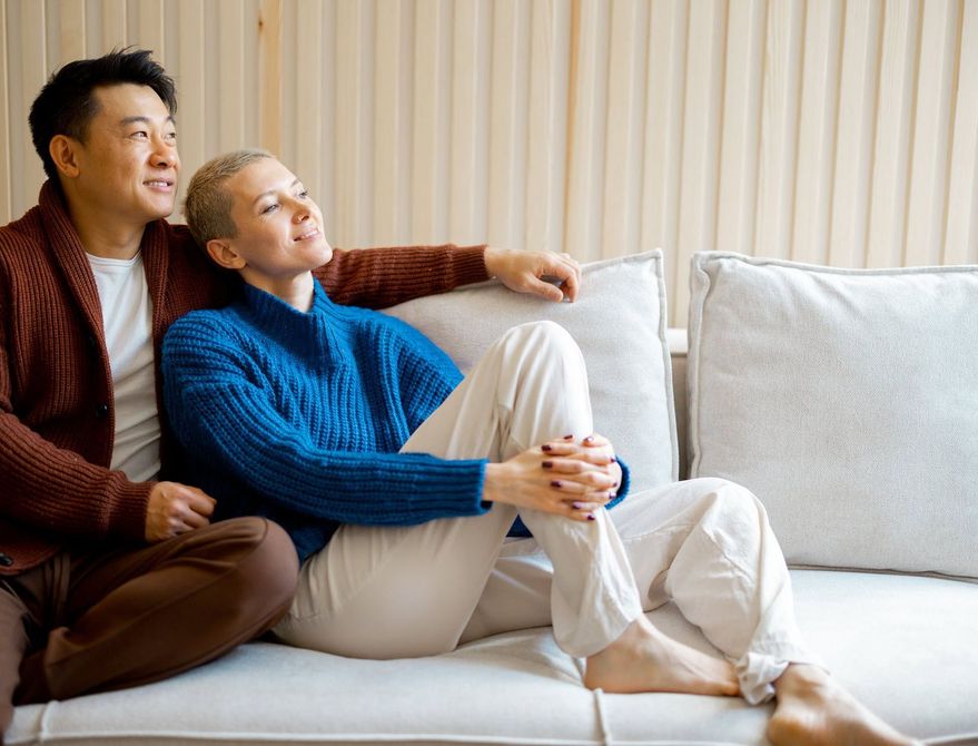 Couple on a couch, both looking up, smiling.