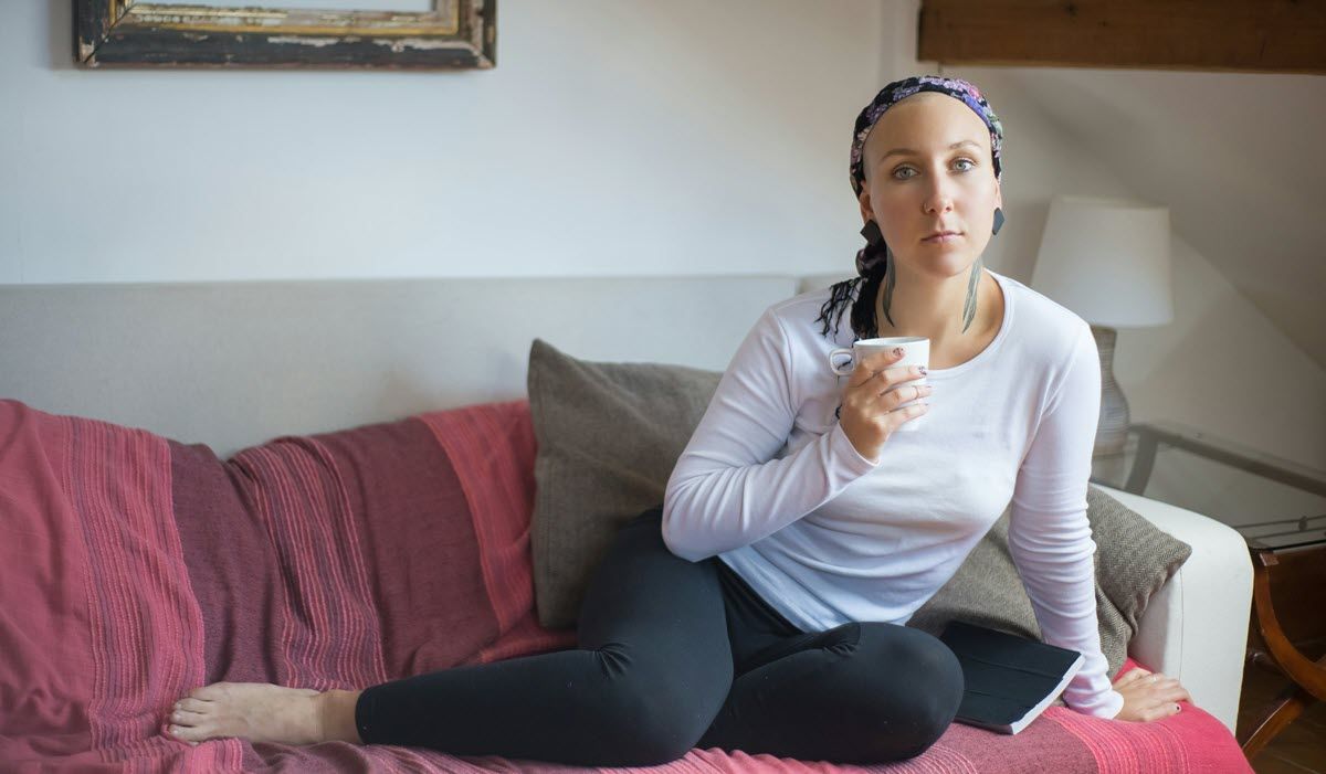 Woman sitting on a couch, holding a drink and looking at the camera.