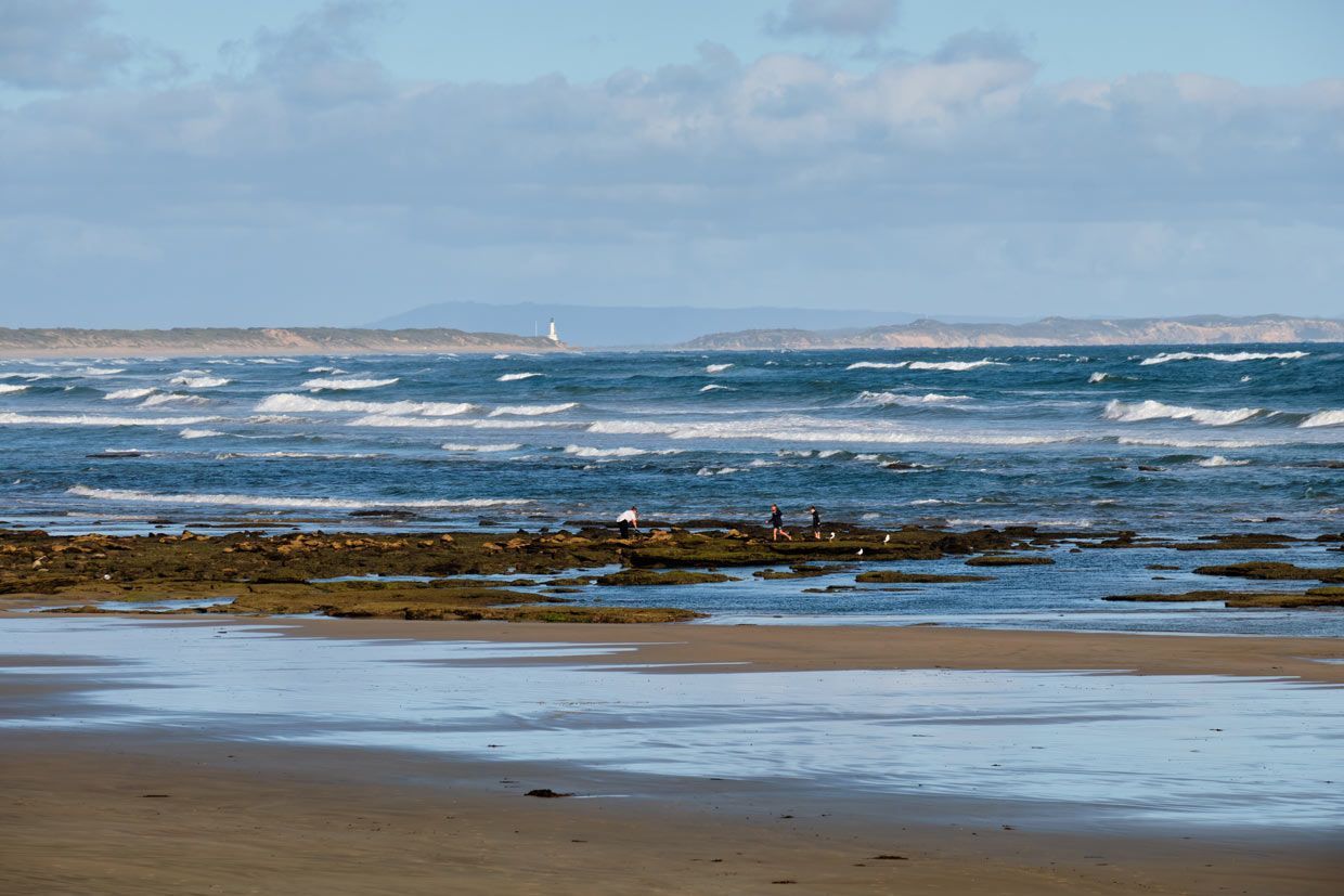A Beach With a Boat in the Distance and Waves Crashing on the Shore — Sunworks Eco Plumbing In Ocean Grove, VIC