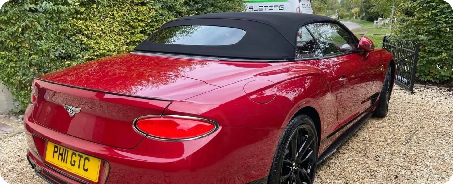 A red Bentley convertible parked on a gravel driveway with black rims and a black top.