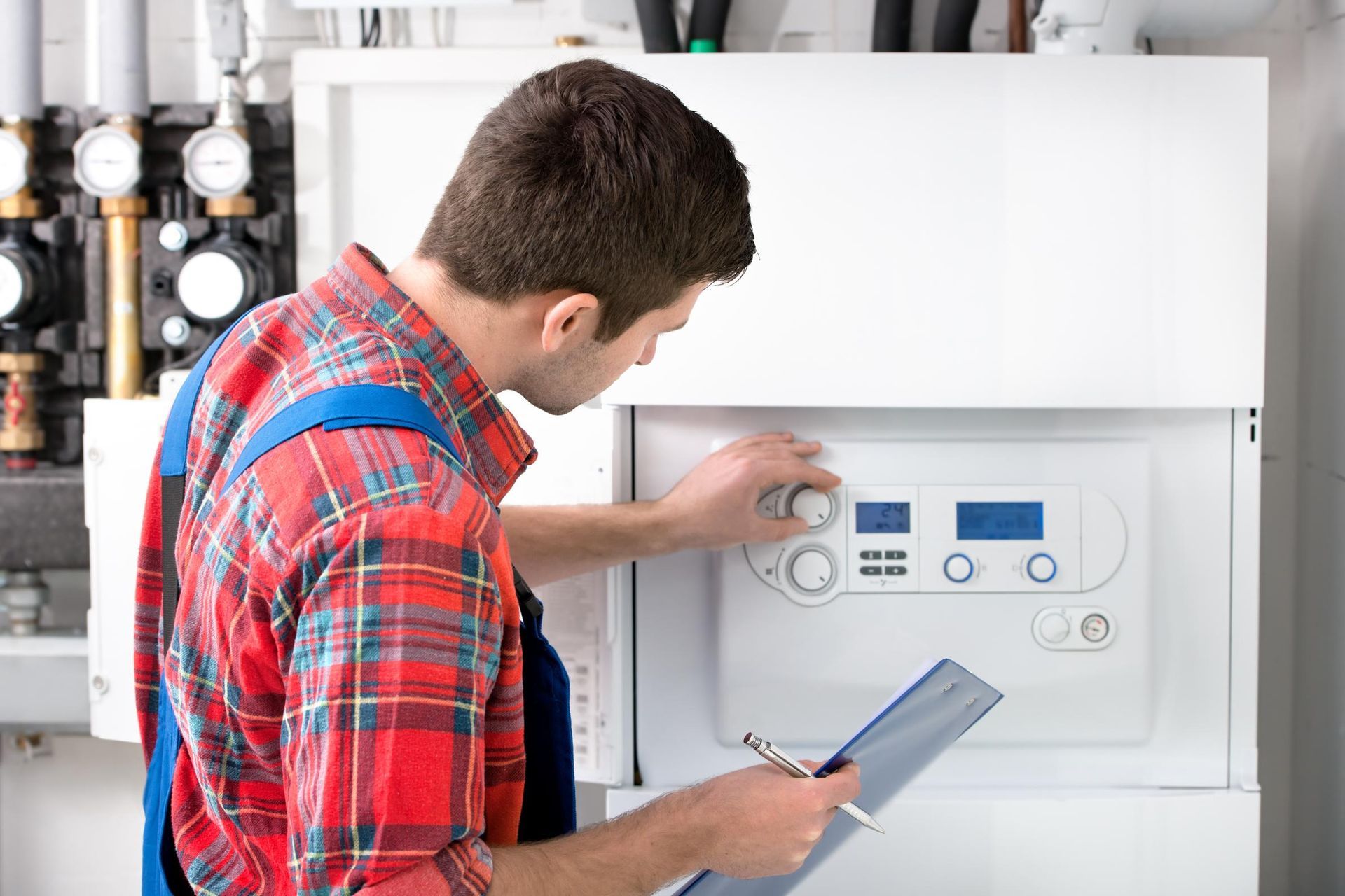 A man is working on a boiler and holding a clipboard.