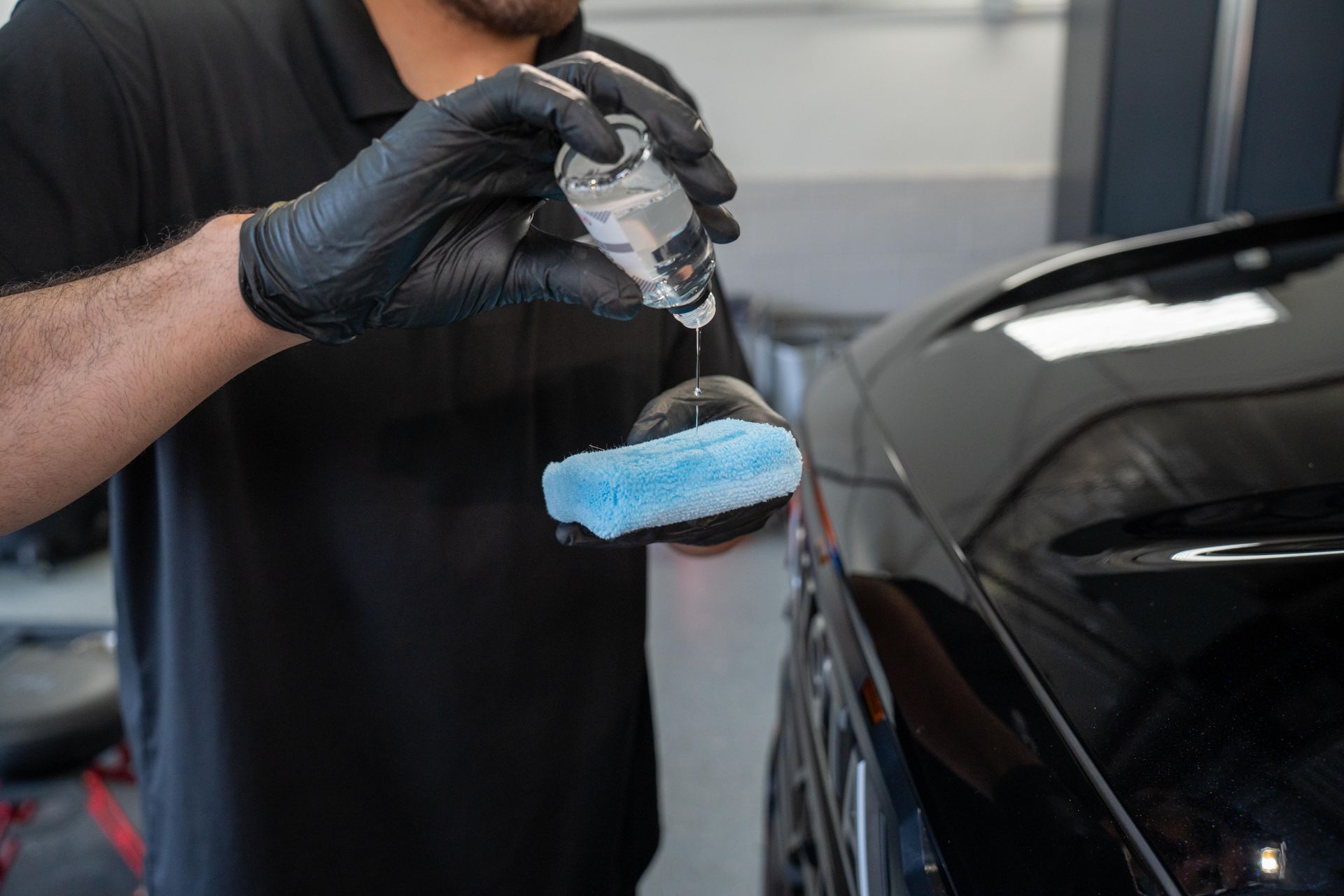 A man is polishing a black car with a sponge and a spray bottle.