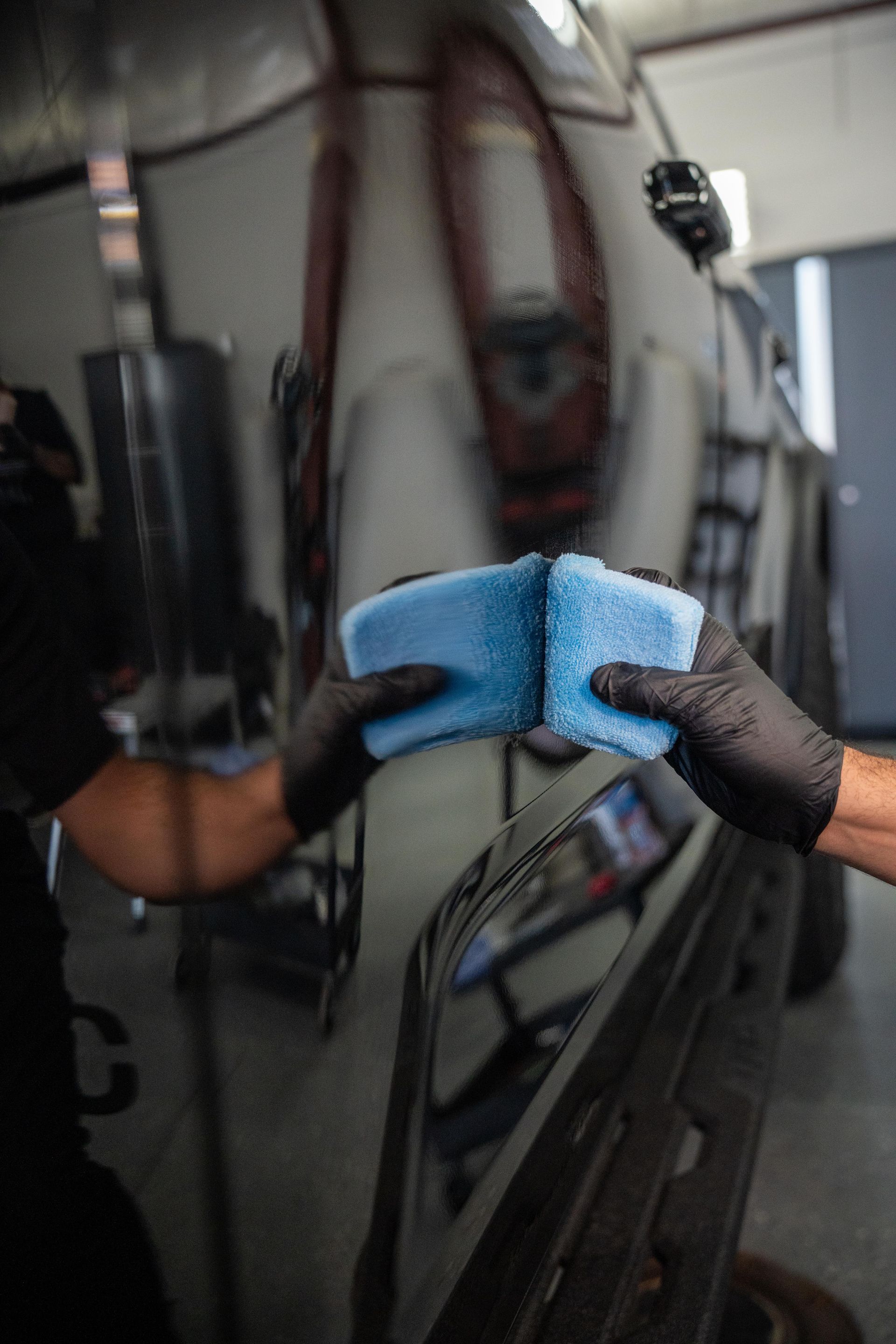 A person is holding a blue sponge in front of a car.