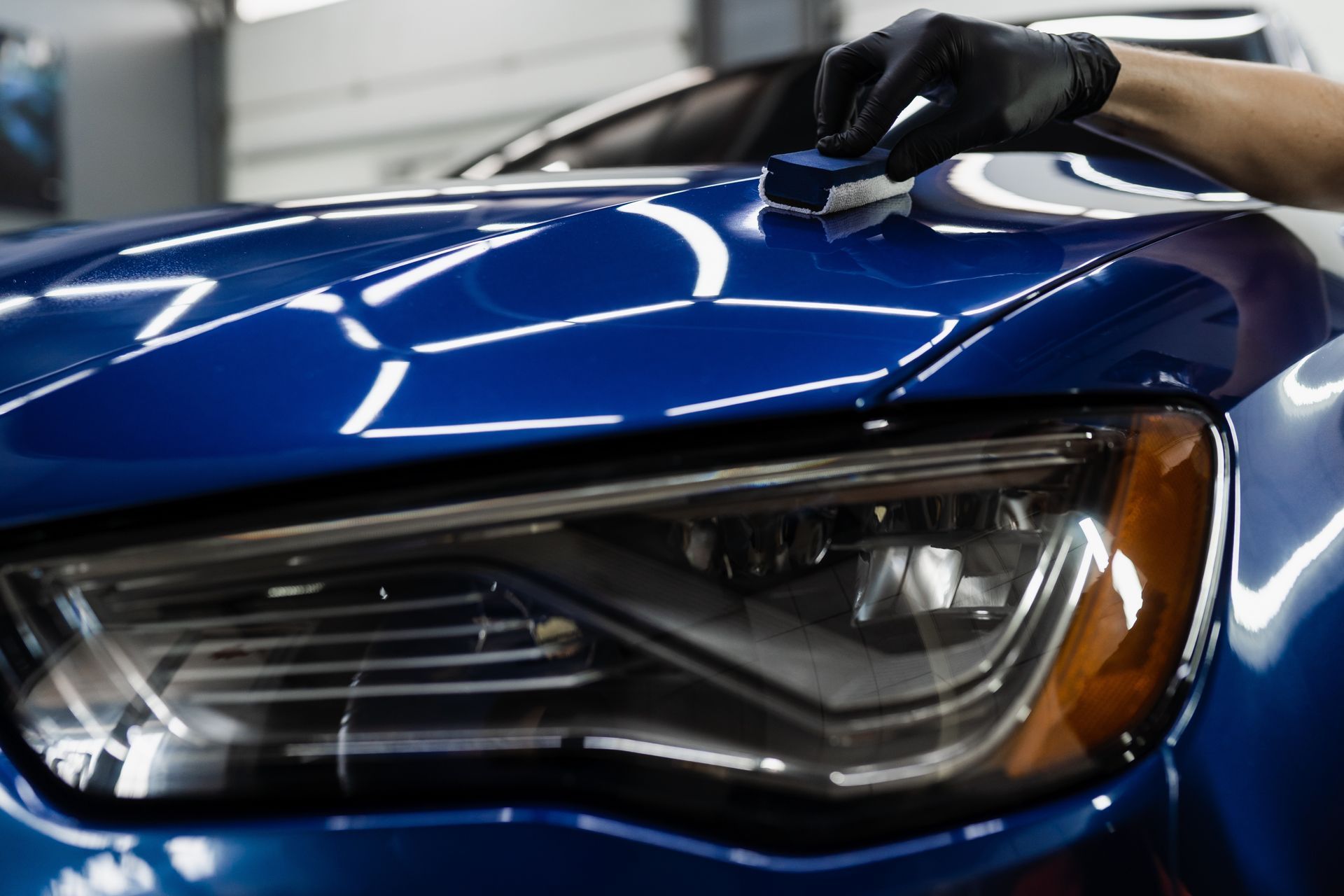 A person is polishing the hood of a blue car.