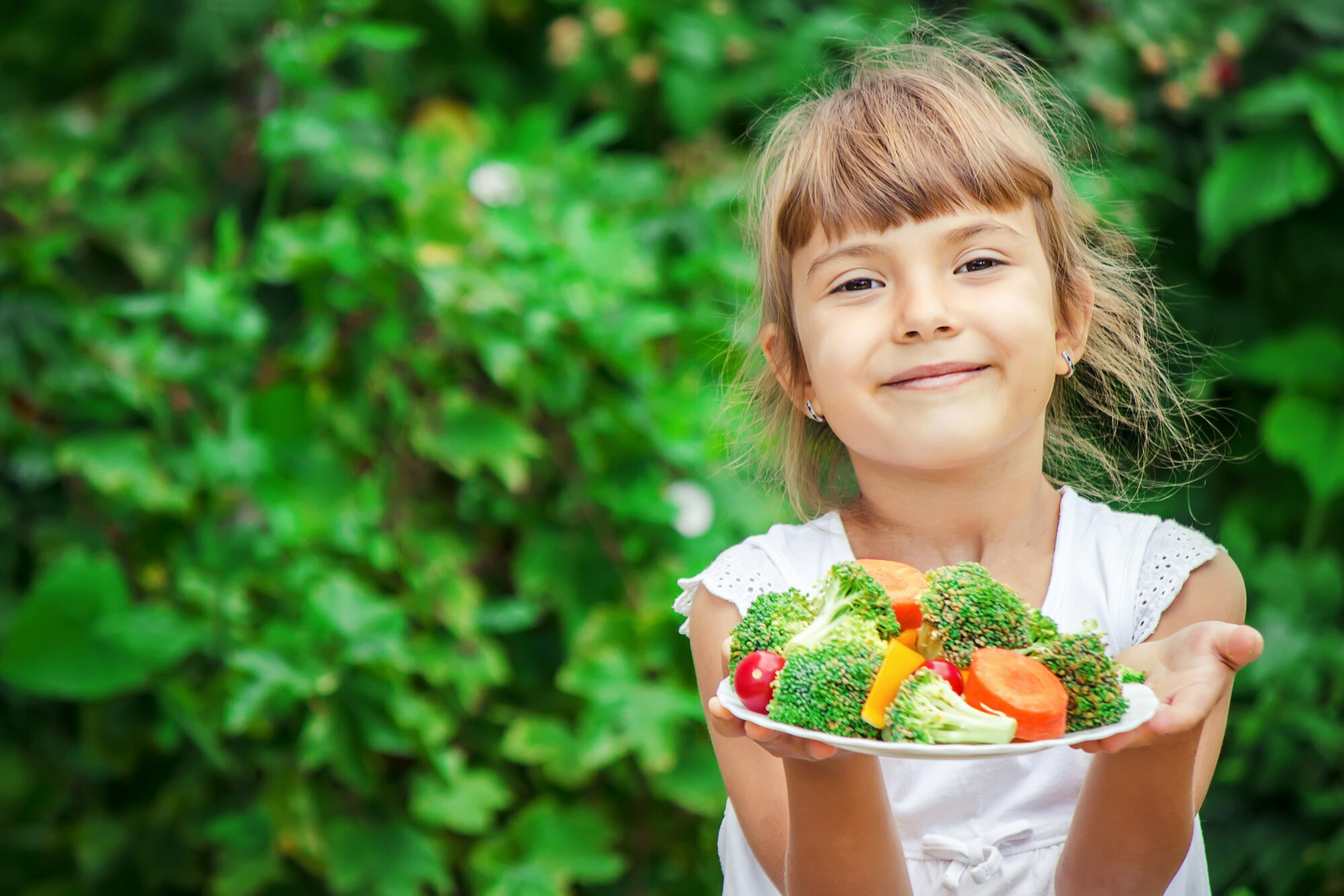 A little girl holds a plate of healthy food for kids made up of vegetables.