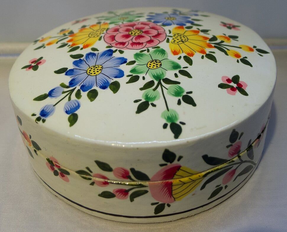 Round, white painted box with colorful floral design on the lid and sides.