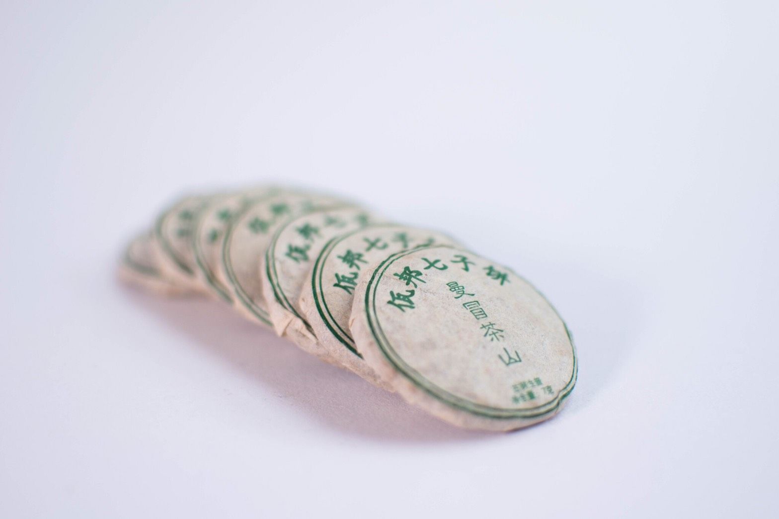 Stack of small, round, beige tea cakes with green Chinese characters printed on them.