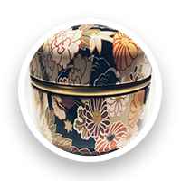 Round decorative container with floral design in gold, cream, and brown on a dark background.