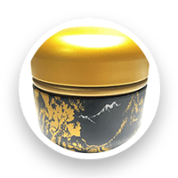 Black and gold container with landscape design, gold lid, on a white circle.