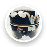 Black lacquerware container with gold trim and painted floral design.