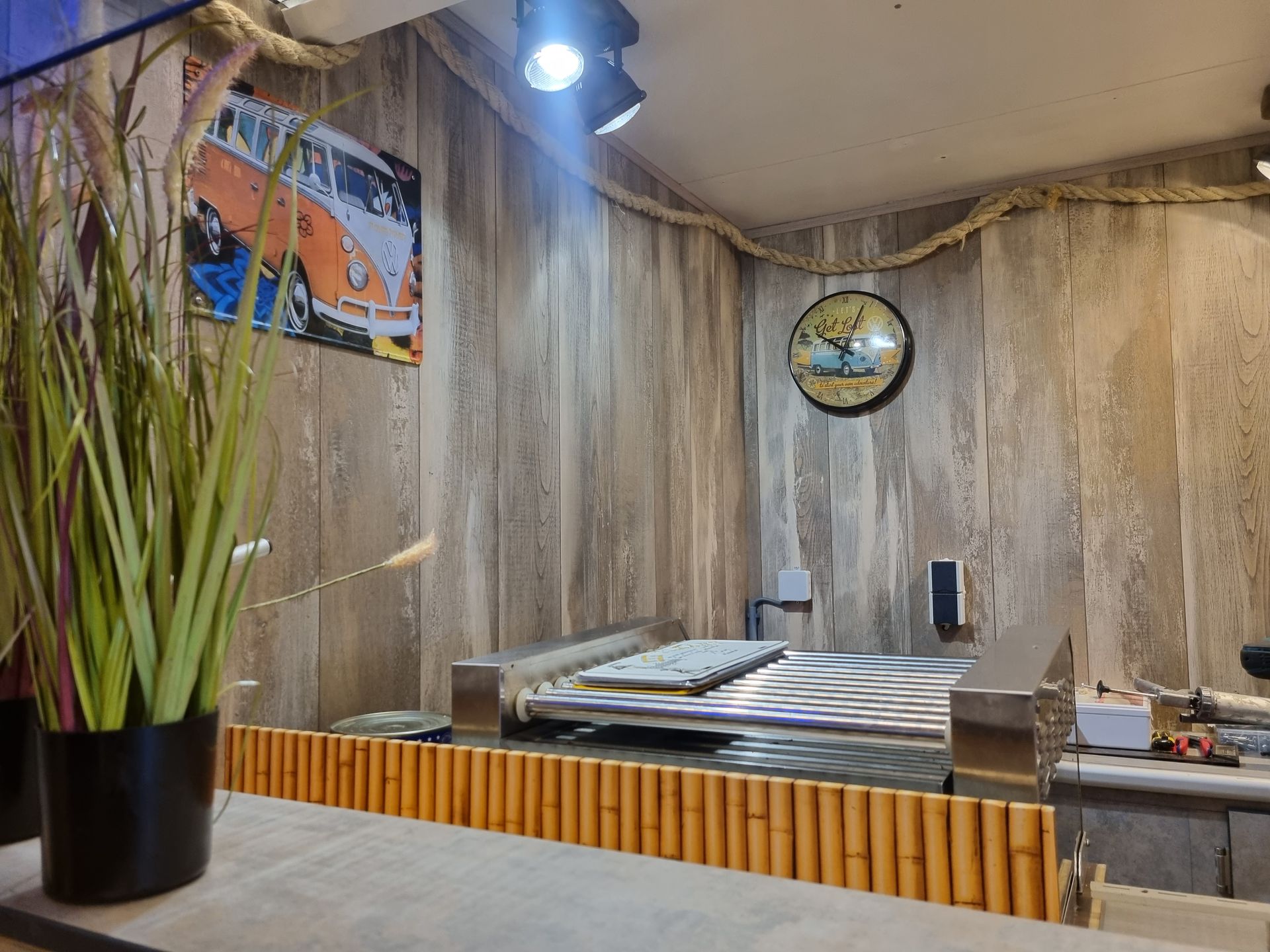 Een restaurantinterieur met een kookoppervlak, bamboe afwerking, een kunstwerk van een VW-busje en een klok.