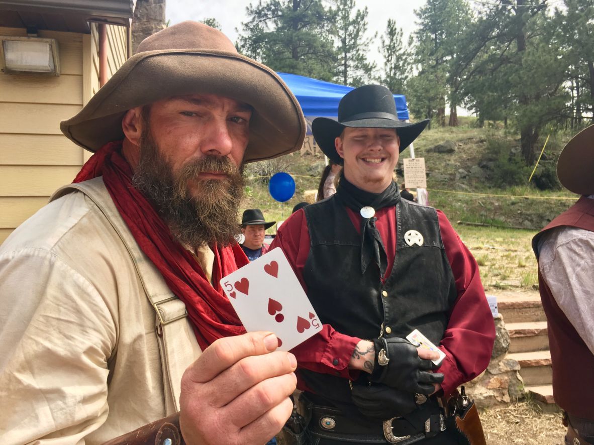 A man in a cowboy hat is holding a playing card with hearts on it.
