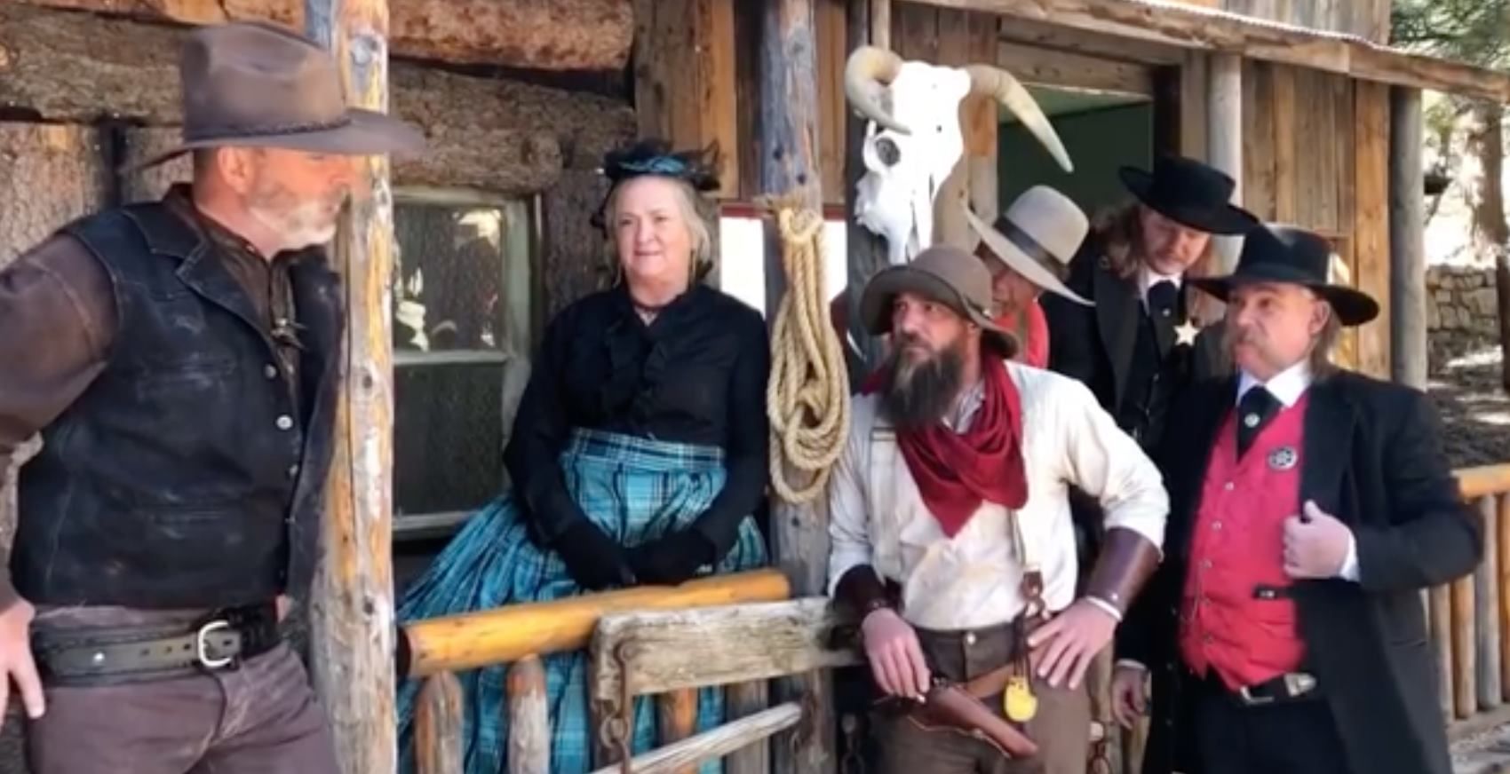 A group of cowboys and a woman are standing on a porch.