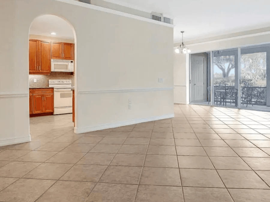 An empty room with a tiled floor and a kitchen in the background.