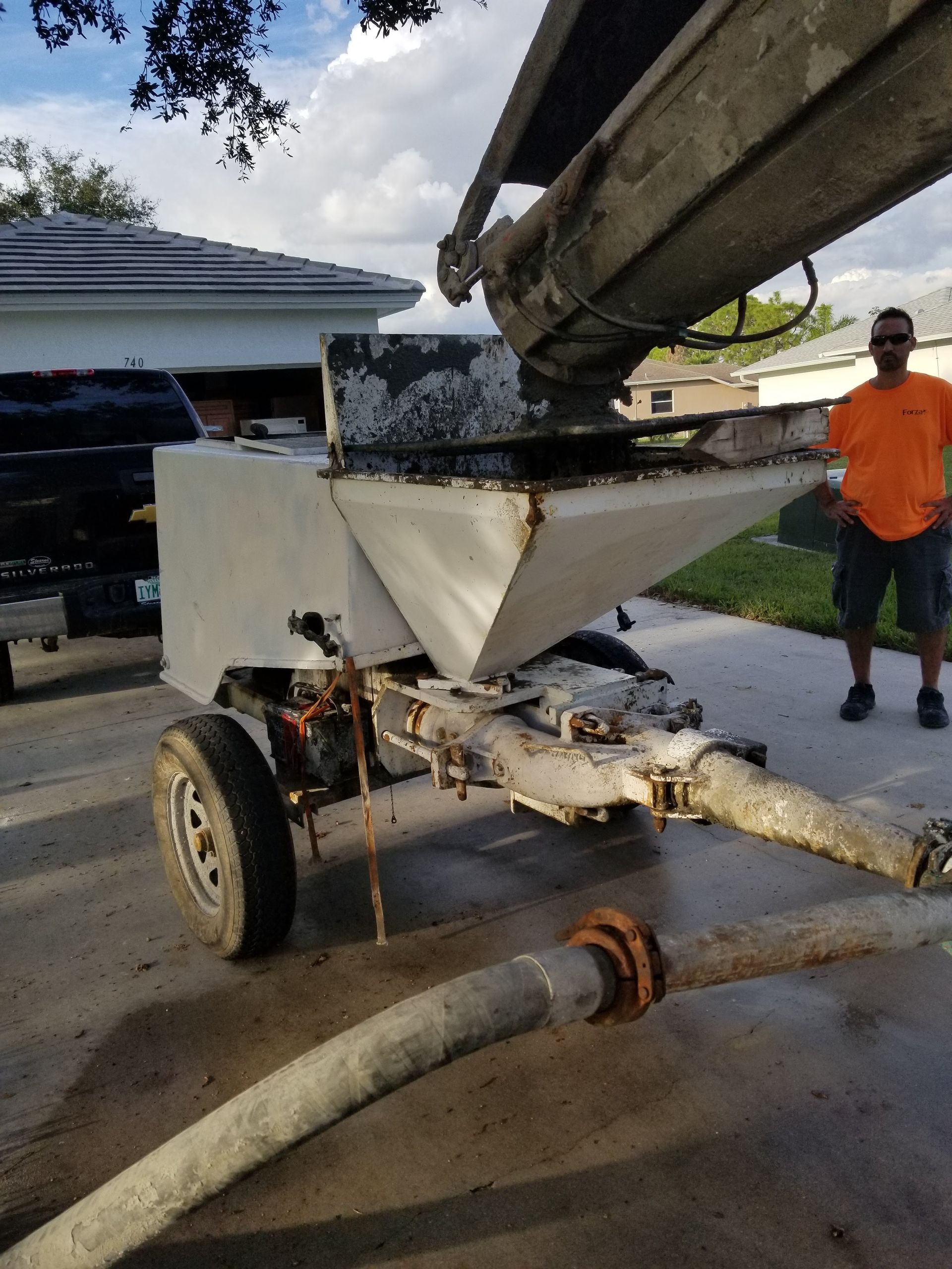 A man in an orange shirt is standing next to a concrete pump.
