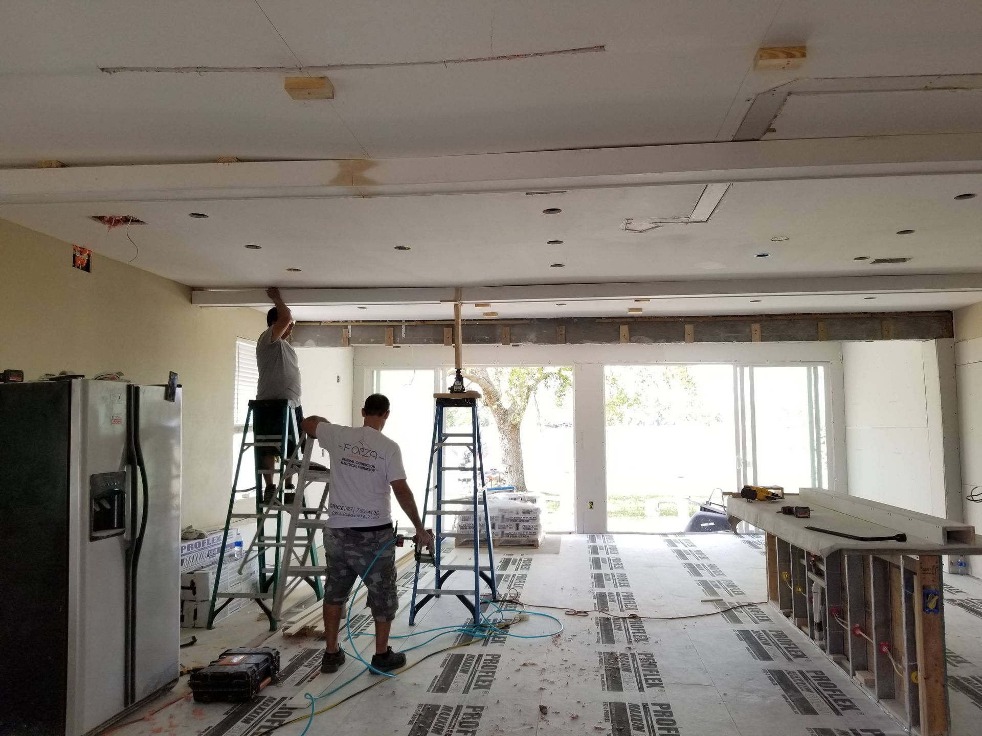 Two men are working on a ceiling in a room.