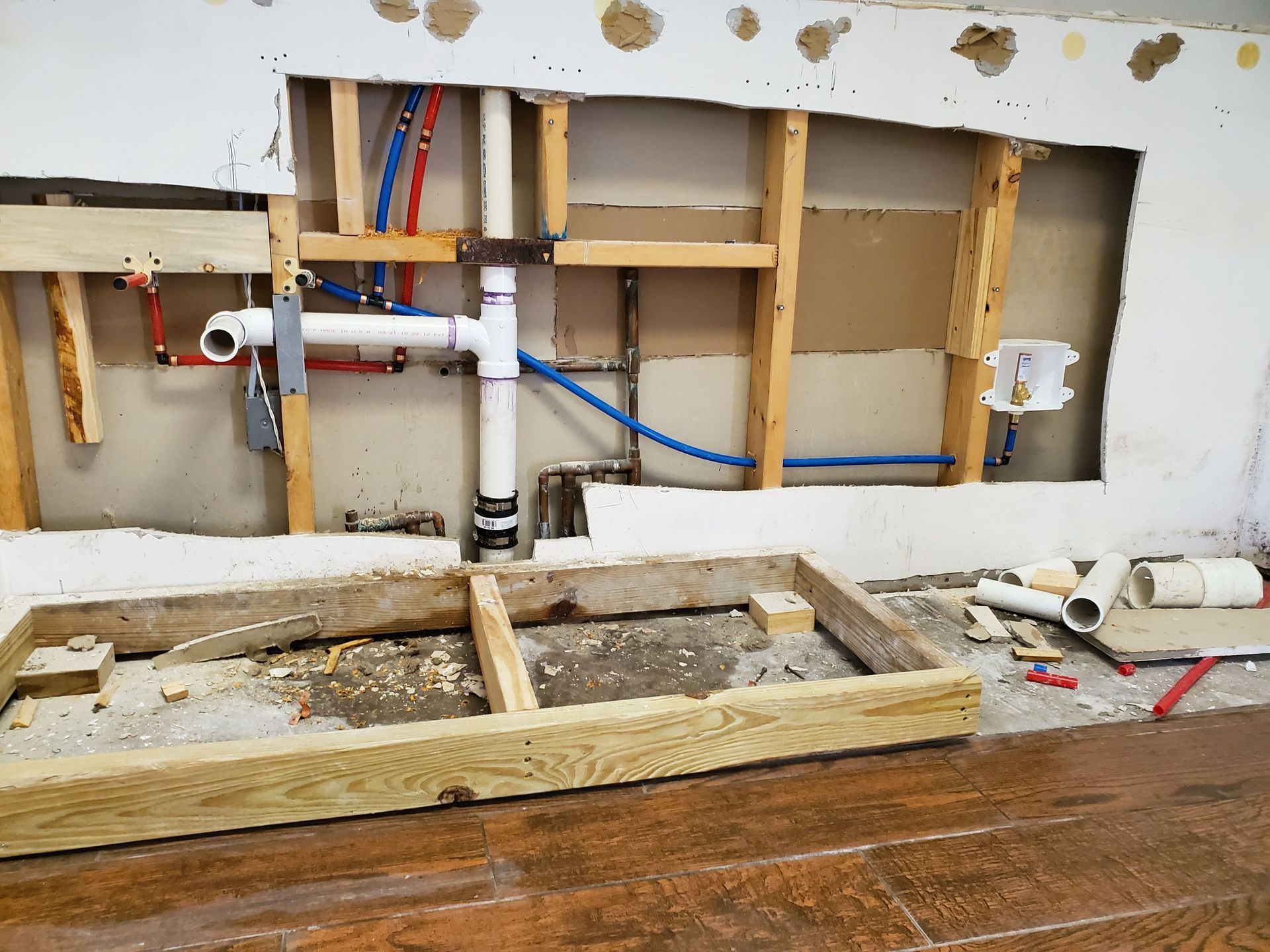 A wooden frame is sitting on the floor next to a wall with pipes coming out of it.