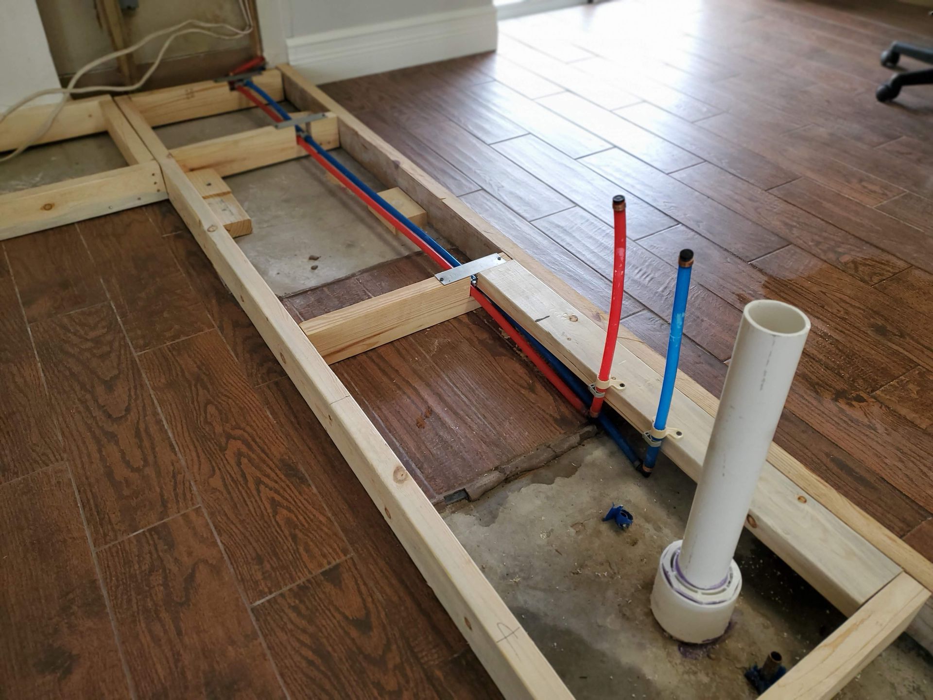 A wooden frame with pipes coming out of it is sitting on a wooden floor.
