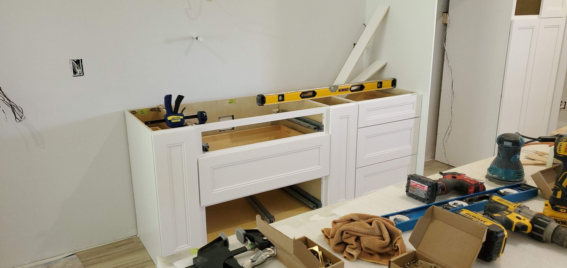 A kitchen cabinet is being built in a room with tools on the floor.