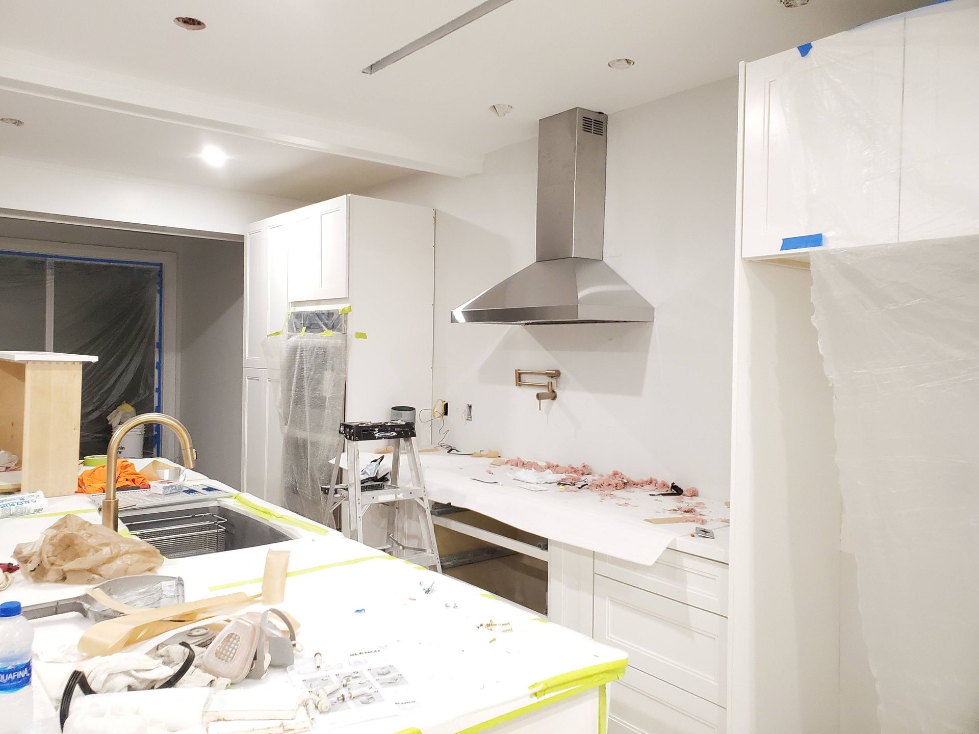 A kitchen under construction with white cabinets and a stainless steel hood.