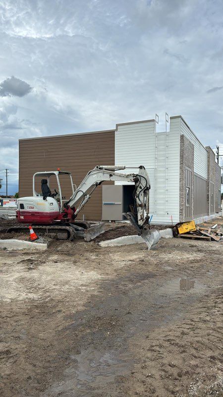 A small excavator is sitting in front of a building under construction.