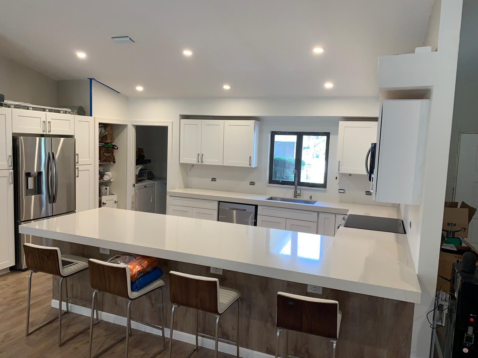 A kitchen with white cabinets , white counter tops , stainless steel appliances and a large island.