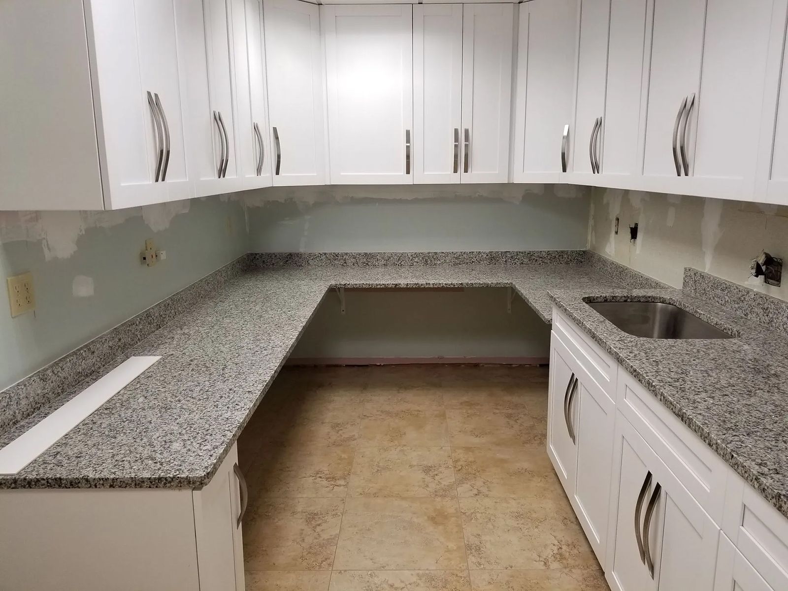 A kitchen with granite counter tops and white cabinets and a sink.