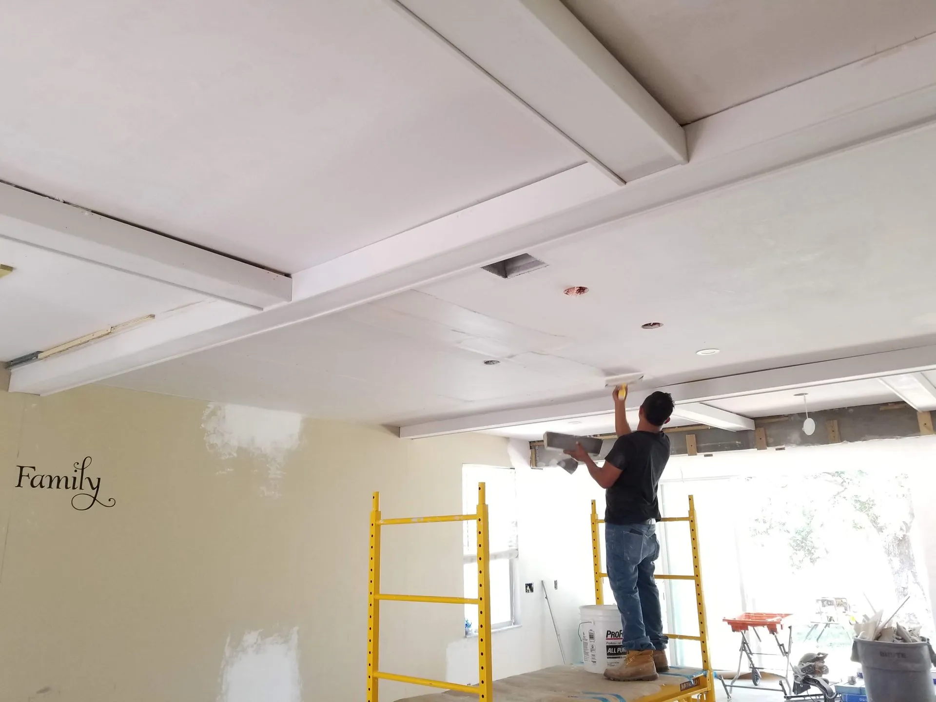 A man is standing on a scaffolding painting the ceiling of a room