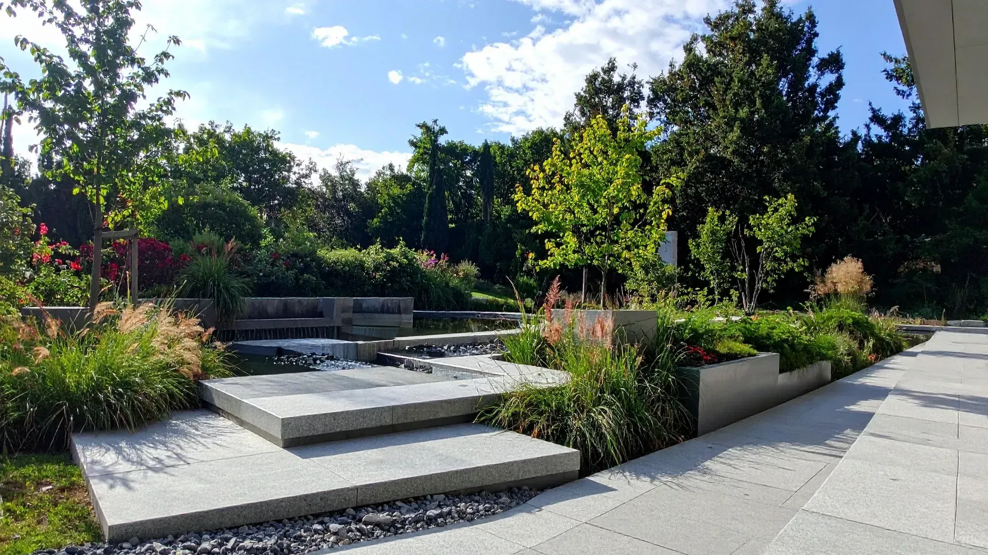 Modern landscaped garden with stone steps, water feature, and lush greenery.