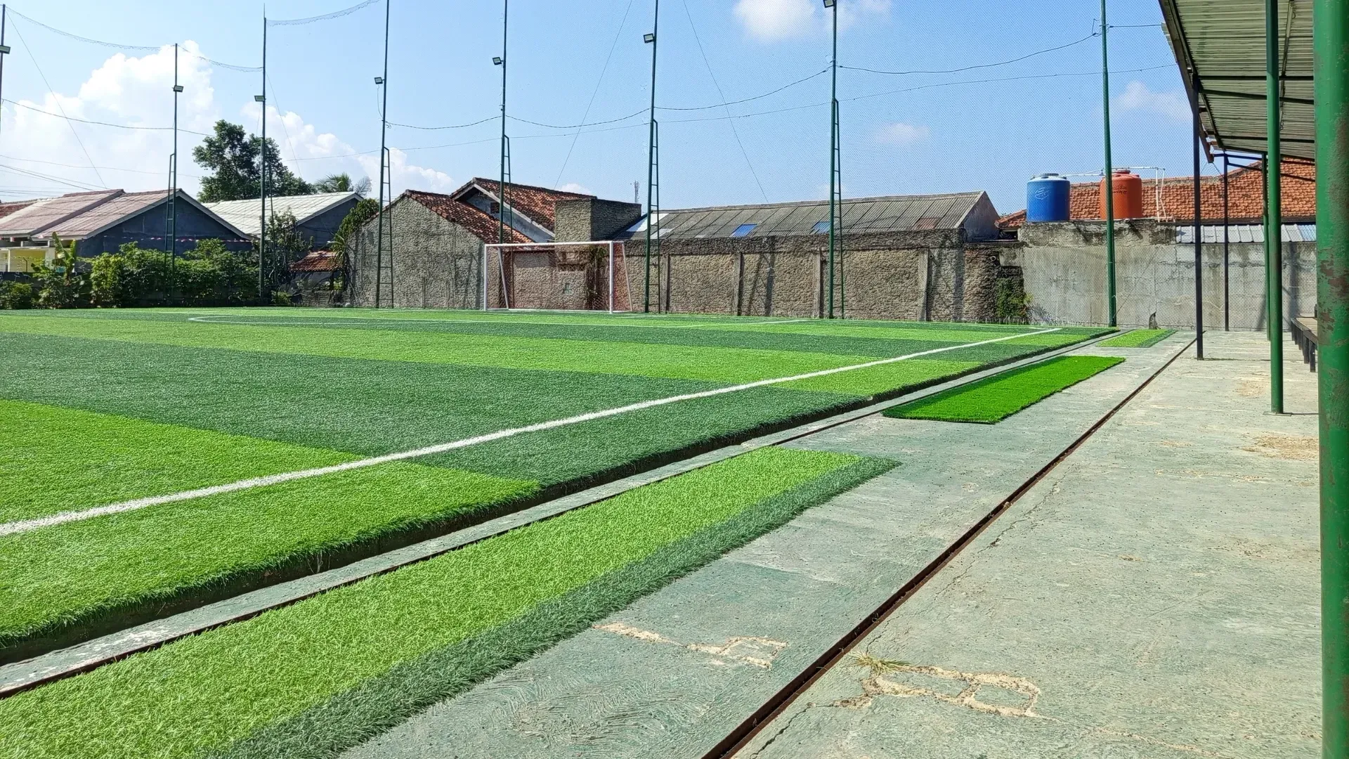 Artificial turf soccer field with netting and brick buildings in the background.