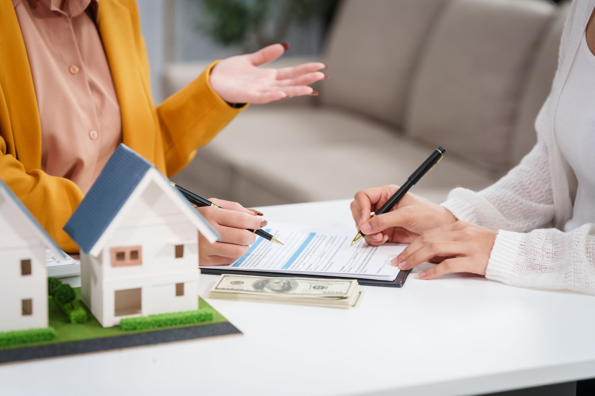 A woman is sitting at a table with a model house and signing a document.