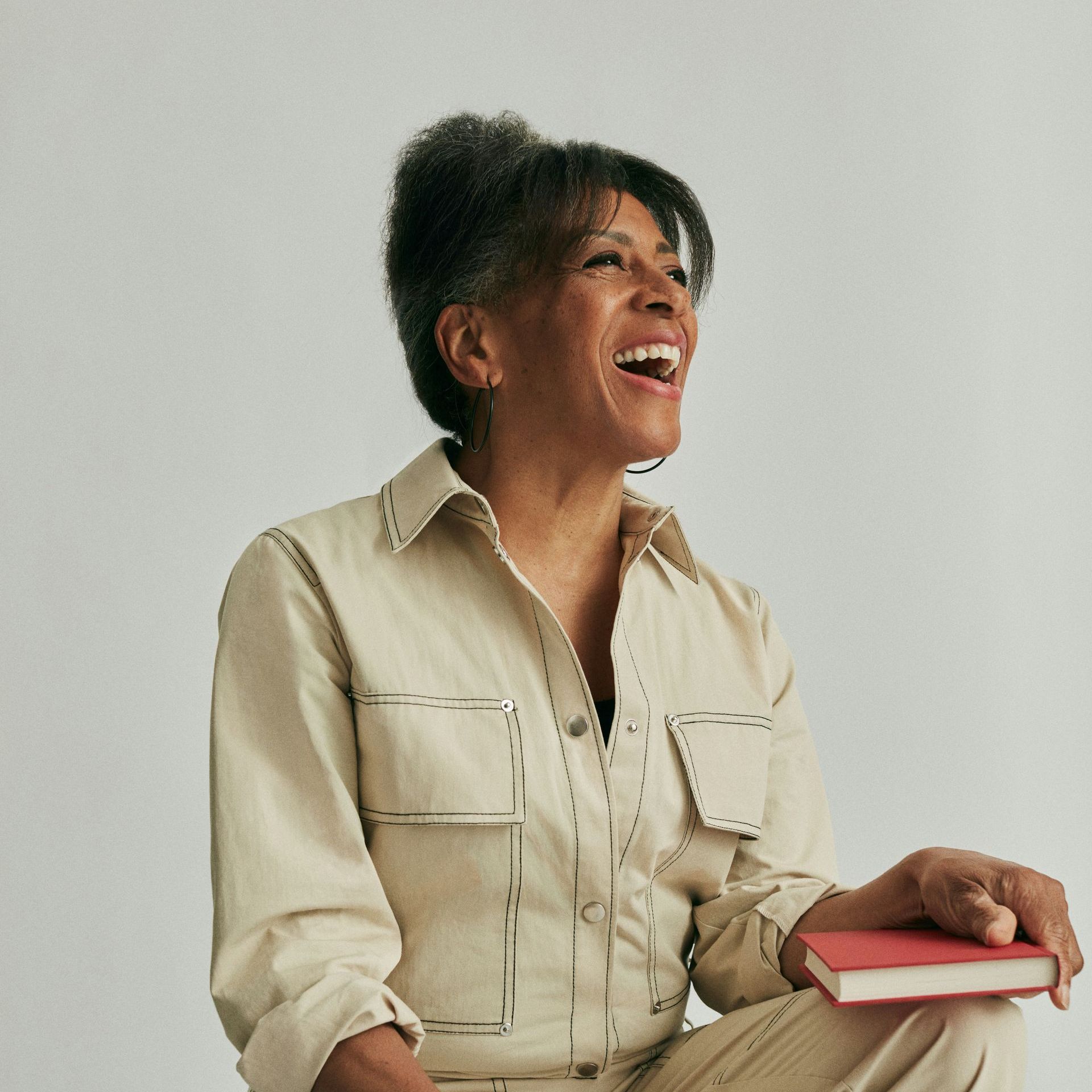 A woman in a tan shirt is holding a book and smiling