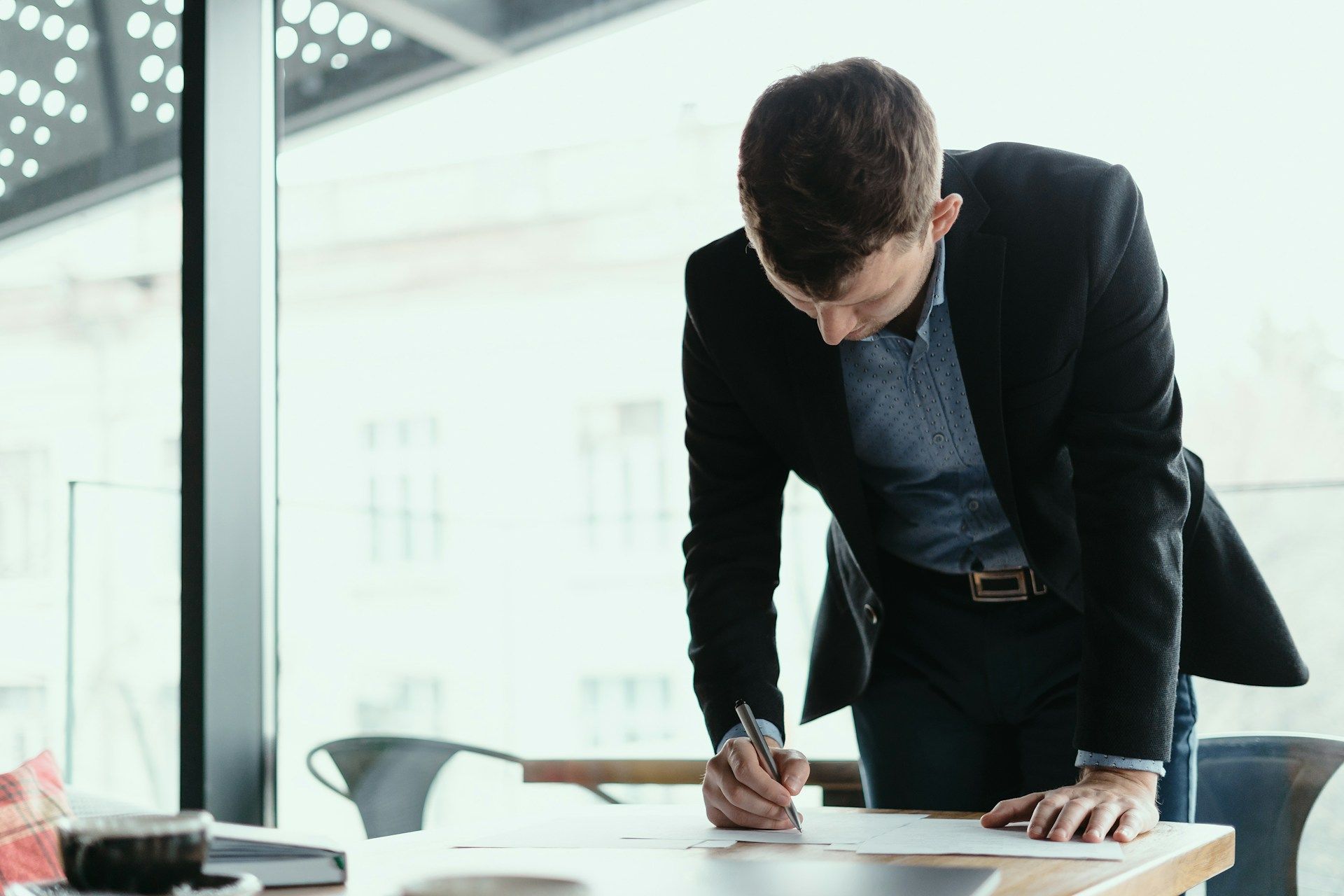 Person's hands using a calculator and writing on paper near a laptop, indoors.