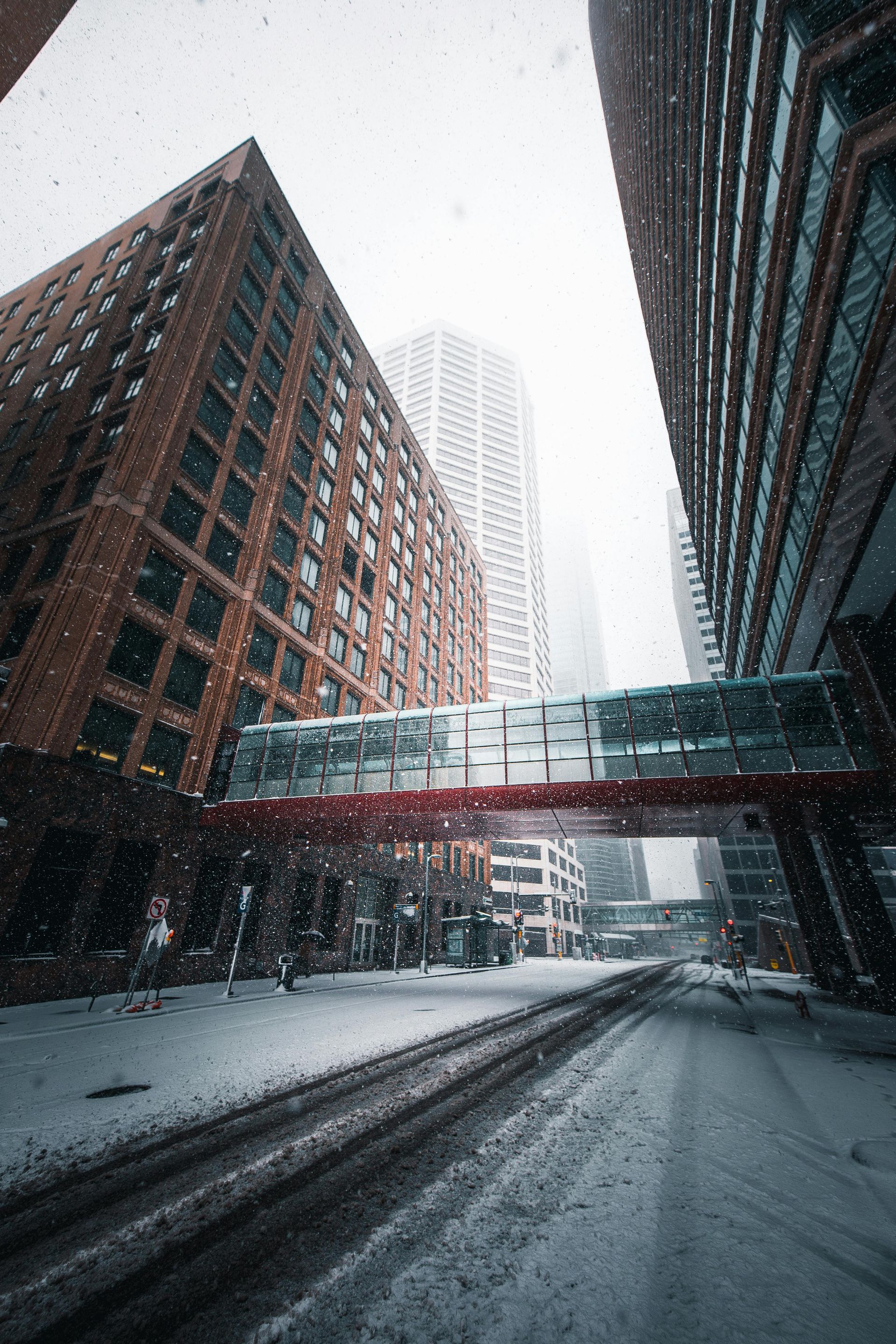 Snowy urban street with brick buildings and a skyway connecting them.