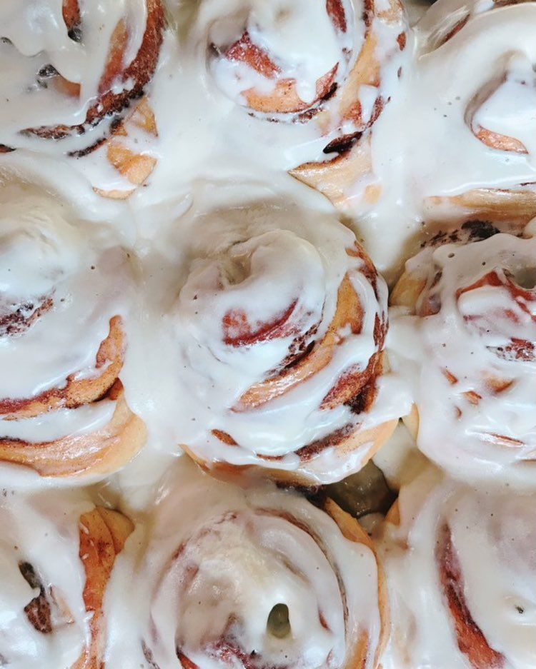 A close-up of several swirled cinnamon rolls covered in a thick, white cream cheese icing.