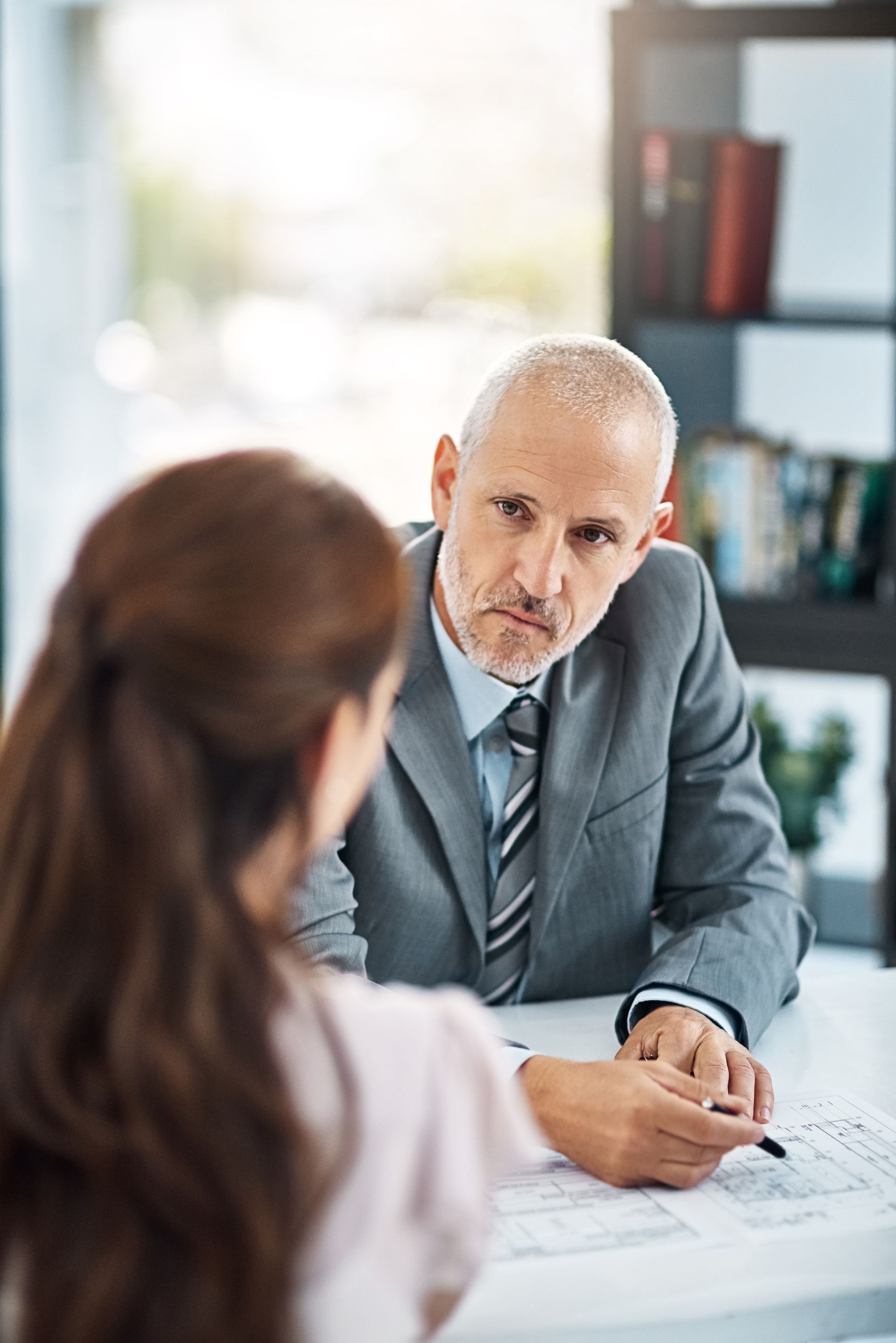 Two people in a business meeting, one man in a gray suit speaking across a desk