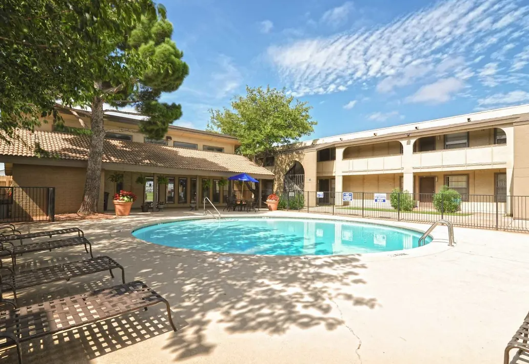 Outdoor pool area at an apartment community with lounge chairs and surrounding building.