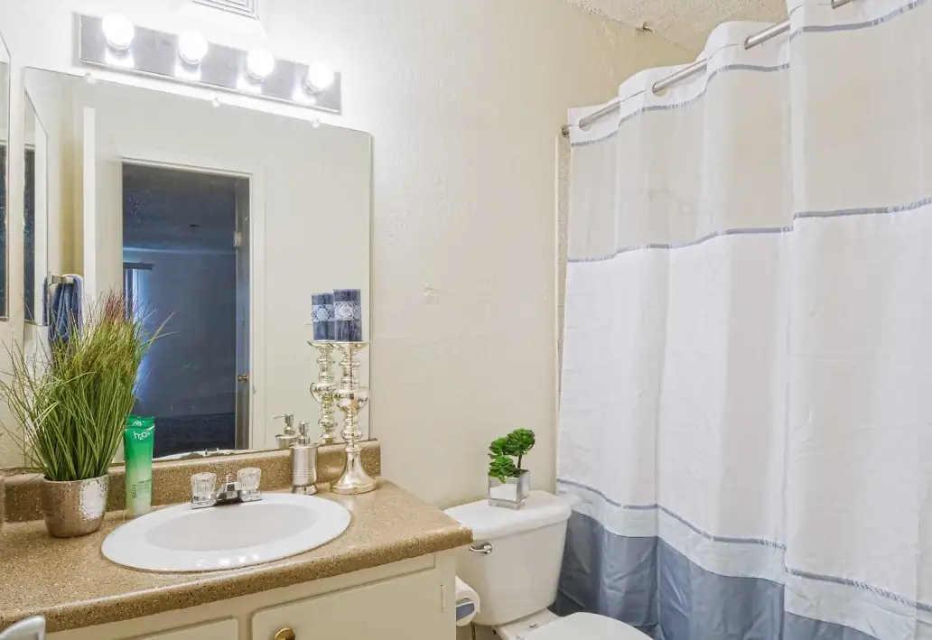 Bathroom in an apartment with a vanity, sink, mirror with lights, toilet, and striped shower curtain.