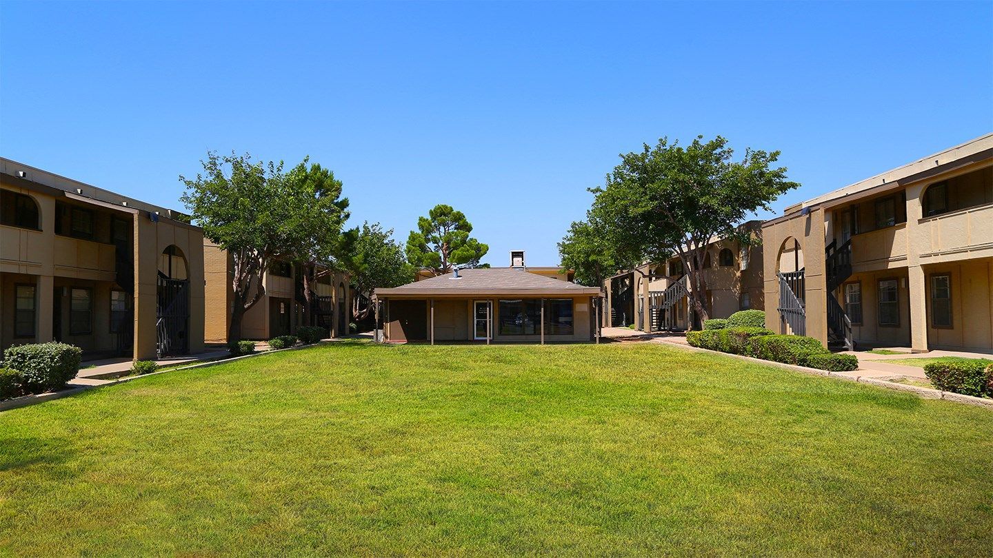 Exterior view of a beige, two-story apartment community arranged around a central grassy courtyard.