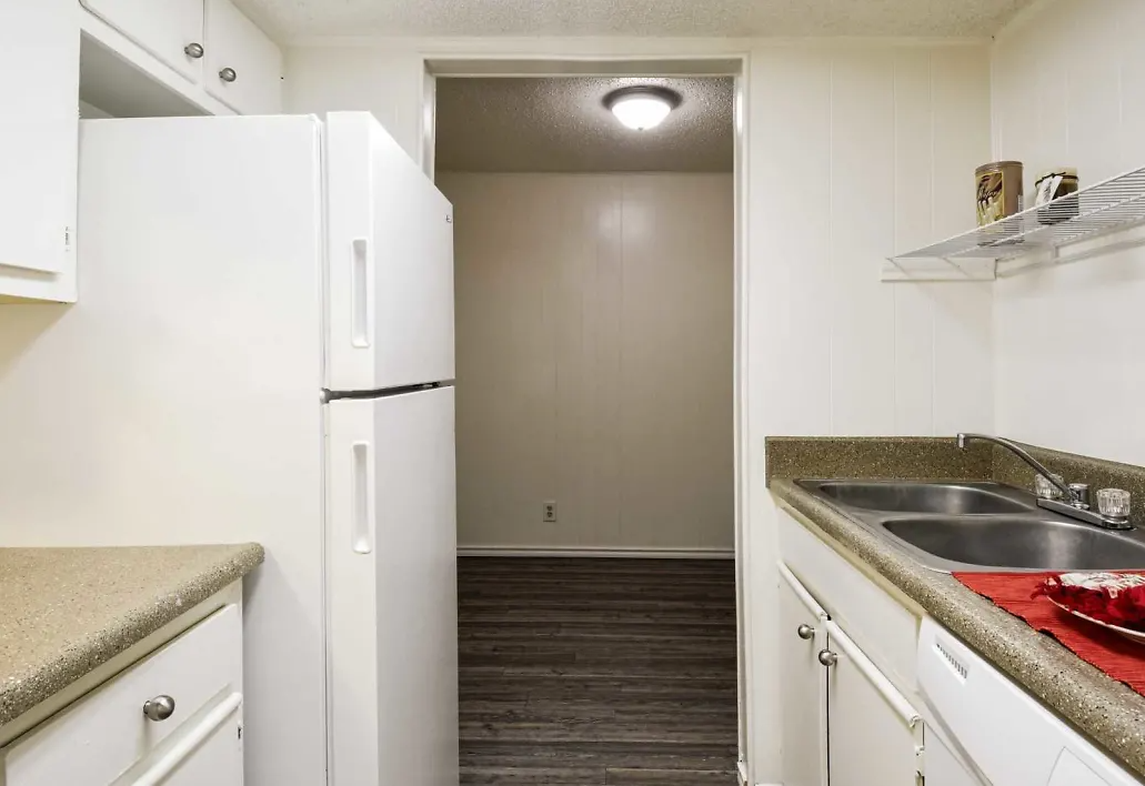 Compact apartment kitchen with white cabinets, fridge, sink, and laminate countertops.