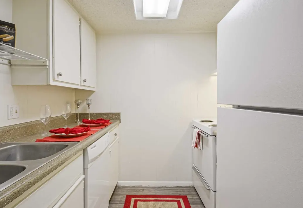 Galley-style apartment kitchen with white cabinets, sink, stove, and refrigerator.