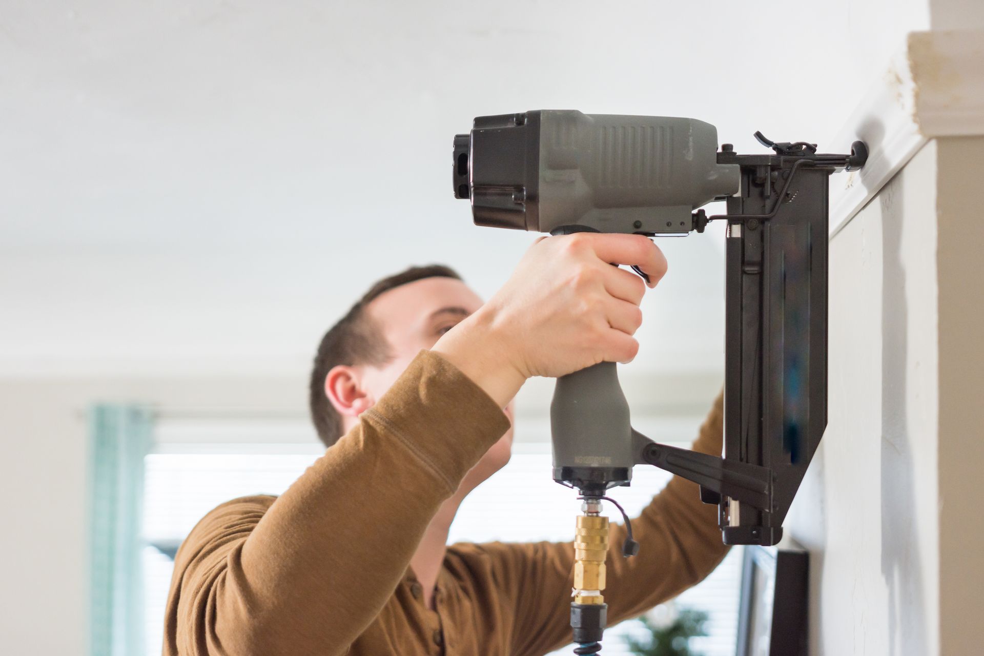 Young father uses generic nail gun to fasten white trim to wall