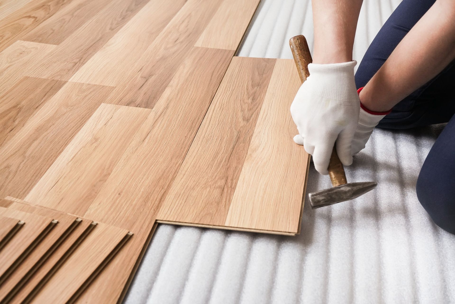 A person is installing a wooden floor with a hammer.